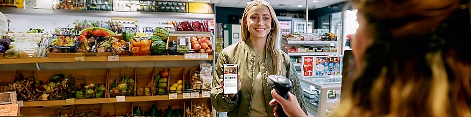 Lächelnde Frau vor Shell Kasse lässt Ihr Smartphone von der Shell Mitarbeiterin scannen